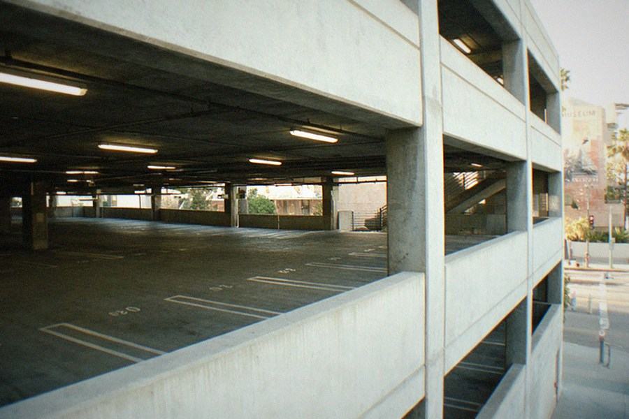 A multi-level parking structure entrance with a ticket machine and signage at the base of a hill