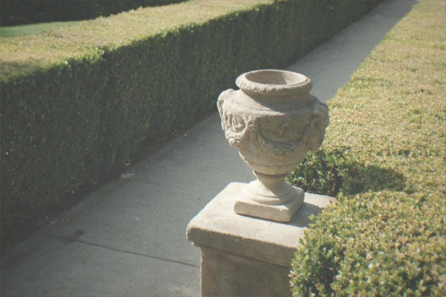 A garden courtyard with sculpted hedges, a stream and stone paths beside white museum buildings