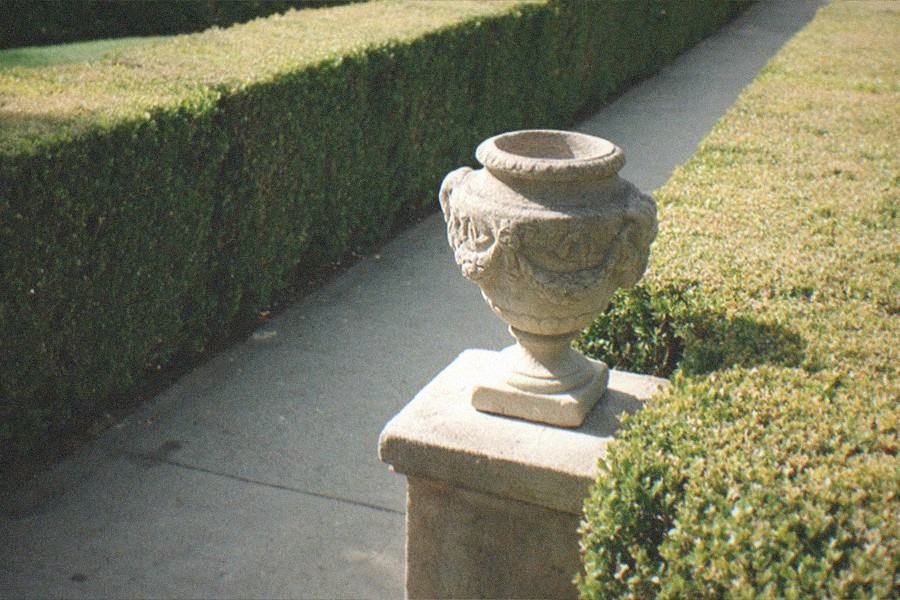 A garden path beside a historic estate building with tall hedges